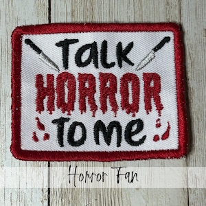 May include: Embroidered patch with a white background, red border, and the text "Talk Horror To Me" in black and dripping red letters. Two knives are positioned above the text. The words "Horror Fan" are written below.