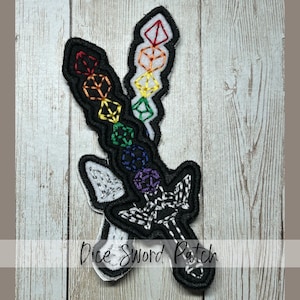 May include: Embroidered patch featuring two stylized swords with dice-shaped designs in a rainbow of colors. The swords have black outlines and white stitching details. The text "Dice Sword Patch" is at the bottom.