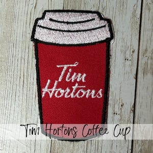 May include: Embroidered patch featuring a red coffee cup with the Tim Hortons logo in white. The cup has a white rim and a black outline. The text "Tim Hortons Coffee Cup" is below the cup.