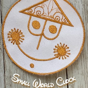 May include: Embroidered patch featuring a stylized clock face design with a triangular roof and sunburst accents. The patch is white with gold-colored embroidery and the text "Small World Clock".