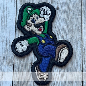 May include: Embroidered patch featuring Luigi from the Super Mario Bros. series. The patch depicts Luigi in his signature green hat, blue overalls, and white gloves, with the name "Luigi" embroidered at the bottom. The patch has a black border.