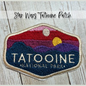 May include: Embroidered patch featuring a desert landscape with two suns and the text "TATOOINE NATIONAL PARK." The patch has a cream-colored border and the words "Star Wars Tatooine Patch" above the design.