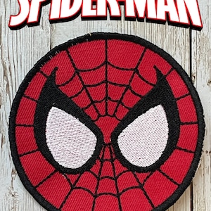May include: A round, red Spider-Man patch with a black spiderweb design and white eye shapes. The patch has a black border and the word "SPIDER-MAN" in white letters with a red outline above it.