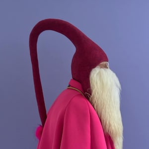 May include: A person wearing a bright pink coat with a long, burgundy felt hat with a long tail. The hat has a white fur trim around the face.