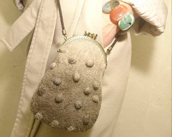 May include: A gray felt purse with a round shape and a clasp closure. The purse has a brown strap and is decorated with small, round, silver embellishments.