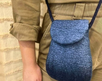 May include: A small, navy blue crossbody bag with a textured, fuzzy exterior. The bag has a flap closure and a long, dark blue cord strap. The bag is worn over a tan jumpsuit.