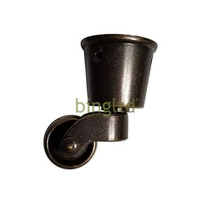 May include: A bronze swivel caster with a round wheel and a cup-shaped base. The caster is designed to be attached to furniture.