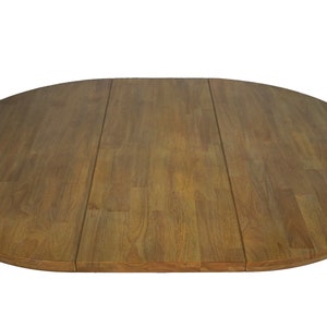 May include: Oval wooden table with a warm brown finish. The tabletop is made of three sections of wood, with visible grain patterns. The table is designed for dining or other household use.