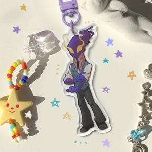 May include: A selection of decorative accessories, including a star-shaped keychain, a character keychain, a white cat figurine, and a star charm. The items are arranged on a white surface with star-shaped confetti scattered around.