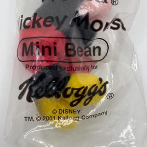 Pu&ograve; includere: Un sacchetto di plastica trasparente contenente un peluche Mickey Mouse Mini Bean. La borsa presenta il testo "World", "Mickey Mouse" e "Kellogg's". Il giocattolo ha elementi rossi, neri e gialli. La borsa &egrave; contrassegnata dai marchi Disney e Kellogg's.