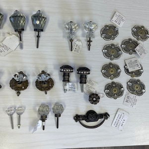 May include: A collection of decorative cabinet hardware, including glass and metal knobs, pulls, and handles. The hardware features various designs, such as faceted glass, ornate metalwork, and rhinestone accents. Ideal for home decor and furniture upgrades.