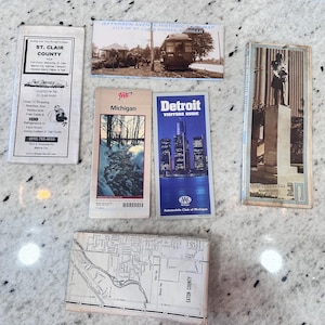 May include: A collection of vintage travel brochures and maps. Includes a St. Clair County brochure, a Jefferson Avenue historic map, a Michigan brochure, a Detroit Visitors Guide, and an Eaton County map.