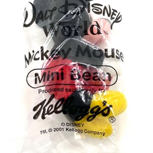 Pu&ograve; includere: Un sacchetto di plastica trasparente contenente mini caramelle a forma di Mickey Mouse. La borsa presenta il logo Walt Disney World, il testo "Mickey Mouse" e il logo Kellogg's. Le caramelle sono rosse, nere e gialle.