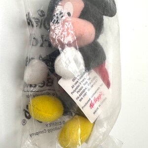 Pu&ograve; includere: Un peluche di Topolino in un sacchetto di plastica trasparente. Il peluche ha testa e orecchie nere, naso rosa e guanti bianchi. La borsa contiene anche forme gialle e bianche. Un'etichetta con testo &egrave; attaccata alla borsa. Fatto in Cina.