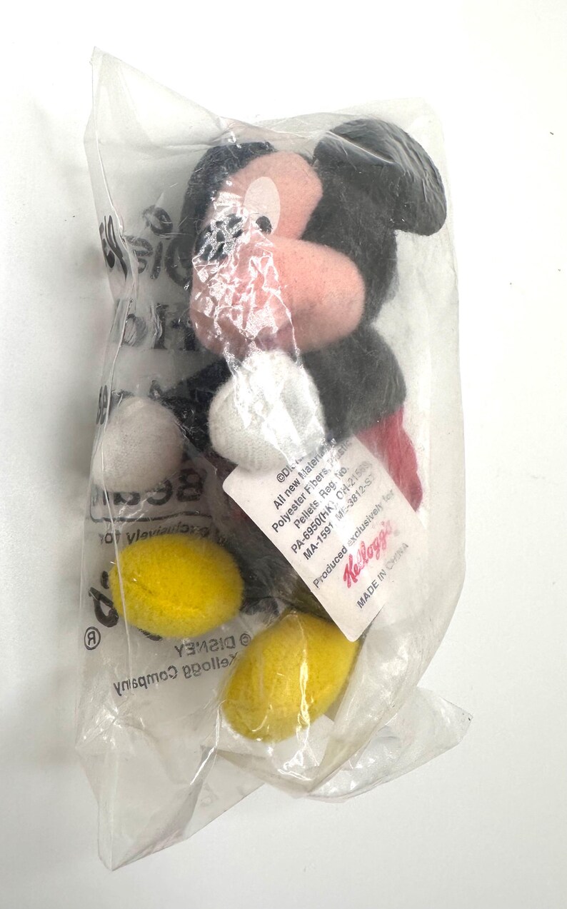 Pu&ograve; includere: Un peluche di Topolino in un sacchetto di plastica trasparente. Il peluche ha testa e orecchie nere, naso rosa e guanti bianchi. La borsa contiene anche forme gialle e bianche. Un'etichetta con testo &egrave; attaccata alla borsa. Fatto in Cina.