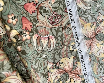 May include: Close-up of fabric with a floral pattern in shades of green, peach, and cream. The design features stylized lilies and foliage. The text "GOLDEN LILY MINOR" BY MORRIS & CO PRINTED IN ENGLAND" is printed on a white strip.