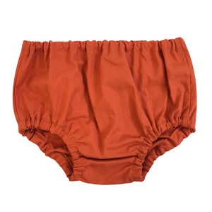 May include: A pair of orange cotton baby bloomers with a gathered elastic waistband.