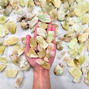 May include: A hand holding a collection of yellow and green crystals. The crystals are rough and have a natural, unpolished look.
