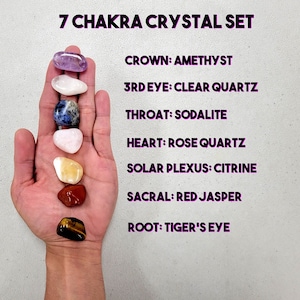 May include: A set of seven chakra crystals, each representing a different chakra. The crystals are arranged in a line, from top to bottom: amethyst, clear quartz, sodalite, rose quartz, citrine, red jasper, and tiger's eye.