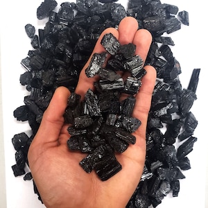 May include: A hand holding a pile of black tourmaline crystals. The crystals are rough and have a natural, unpolished look.