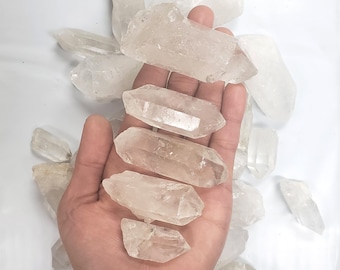 May include: A collection of clear quartz crystal points, some with a slight cloudy appearance, arranged in a hand. The crystals are various sizes and shapes, with some being long and thin, while others are shorter and wider.