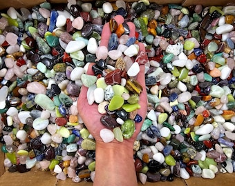 May include: A hand holding a variety of colorful tumbled stones. The stones are small and smooth, and they are arranged in a random pattern. The stones are a mix of different colors, including red, green, blue, and white.