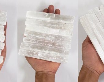 May include: A collection of white selenite sticks, also known as selenite wands, are stacked in three different arrangements. The sticks are smooth and have a natural, white, crystalline appearance.