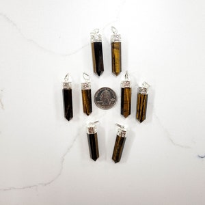 May include: Ten tiger's eye gemstone pendants with silver caps. The pendants are arranged in a star shape with a US quarter for scale.