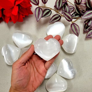 May include: A collection of seven white selenite heart-shaped crystals. The crystals are smooth and polished, with a subtle shimmer.