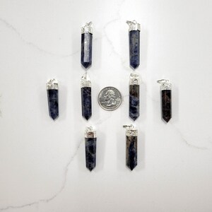 May include: Eight silver and blue gemstone pendants, each with a silver bail. The pendants are arranged in two rows of four, with a US quarter dollar coin for scale.