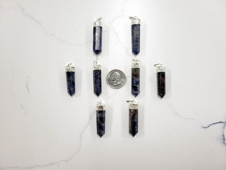 May include: Eight silver and blue gemstone pendants, each with a silver bail. The pendants are arranged in two rows of four, with a US quarter dollar coin for scale.
