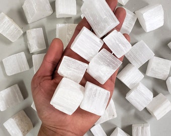 May include: A collection of white selenite crystal cubes. The crystals are smooth and have a striated texture.