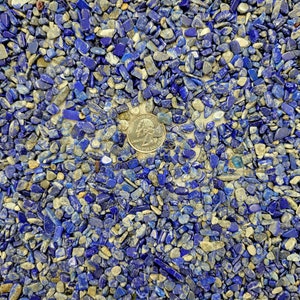 May include: A close-up view of a surface covered in small, blue and gray stones. A silver US quarter is placed in the center of the image.