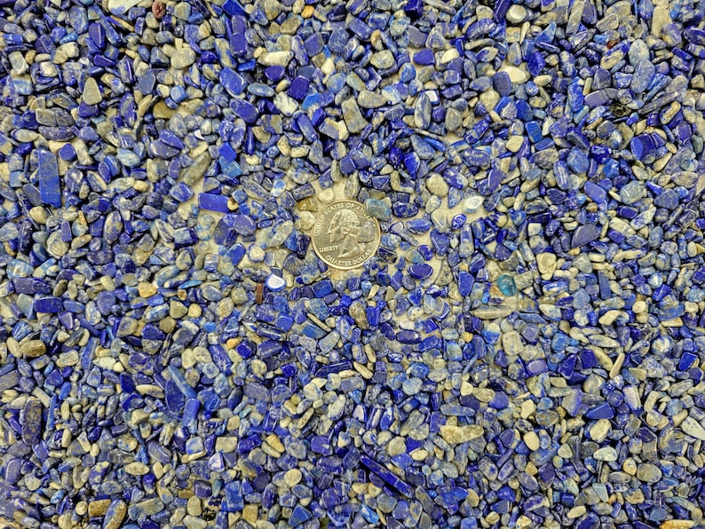 May include: A close-up view of a surface covered in small, blue and gray stones. A silver US quarter is placed in the center of the image.