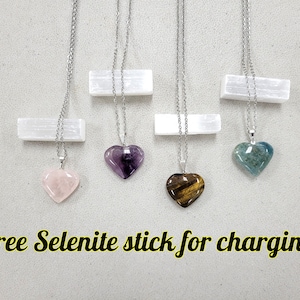 May include: Four silver necklaces with heart-shaped crystal pendants. The crystals are amethyst, rose quartz, tiger's eye, and aquamarine.  Free selenite stick for charging.
