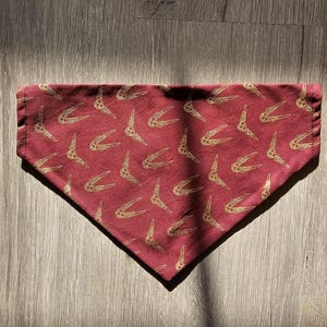 May include: A burgundy bandana with a gold pattern of stylized wings.