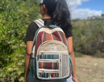 May include: A colorful backpack with a woven design, featuring stripes in red, orange, blue, and green. The backpack has multiple zippered compartments and side pockets. The top of the backpack is beige, and the straps are patterned.