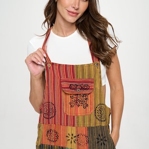May include: Multi-colored striped overalls with a front pocket featuring a button closure and decorative black patterns. The overalls have adjustable straps and a patchwork design on the lower portion.