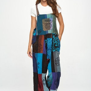 Może przedstawiać: Kombinezon patchwork w odcieniach niebieskiego, turkusowego, brązowego i fioletowego. Szerokie ogrodniczki mają szelki z kieszenią i regulowanymi ramiączkami. Tkanina jest wzorzysta we wzory kwiatowe i paisley. Pod spodem noszona jest biała koszulka.