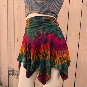 May include: A tie-dye skirt in shades of green, red, orange, and blue. The skirt has a high waist and a flared, asymmetrical hemline. The fabric appears to be soft and flowing, with a unique, colorful pattern.