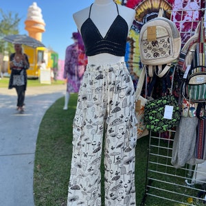 Op de afbeelding: Witte broek met een zwarte paddenstoelprint. De broek heeft een trekkoord in de taille en is op een mannequin. De mannequin draagt een zwart gehaakt haltertop.