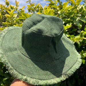 May include: A green, wide-brimmed hat with a frayed edge. The hat is made of a woven material and has a slightly rounded crown.