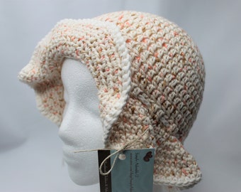 May include: A crocheted baby bonnet in cream and peach with a white crocheted trim. The bonnet is on a white mannequin head. The tag attached to the bonnet reads "Simply Adorable U" and "Handmade with Love & Attention to Detail".