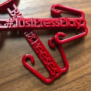 May include: Two red plastic hooks with the text "#JustPressPlay" and "It&Reeses" printed on them.