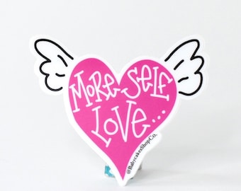 May include: Pink heart-shaped sticker with wings and the text "More Self Love..." and the social media handle "@BabycakesShopCo."