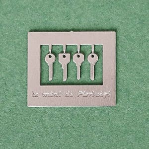 May include: A silver metal bookmark with five keyhole cutouts and the text "Le maître des Pierres".