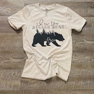 May include: A beige t-shirt with a black bear silhouette and the text "I'm the bigger bear - Beth" printed on the front.
