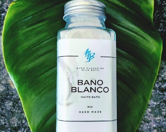 May include: A white glass jar with a silver lid containing a white bath soak. The label reads "Aura Cleansing Milk Bath", "Bano Blanco", "White Bath", "8 oz", and "Hand Made".
