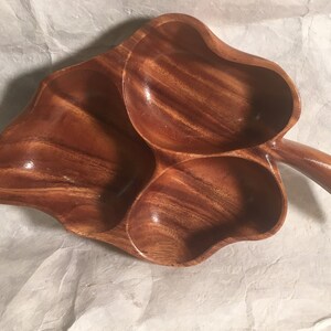May include: A wooden serving dish shaped like a leaf with three separate compartments. The dish is made of dark brown wood with a natural grain pattern.