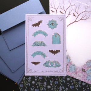 May include: A sticker sheet with gothic-themed illustrations, including bats, an all-seeing eye, and banners with Latin phrases. The stickers are in shades of brown and teal, with the text "PART TIME PRINCESS SHOP" at the bottom.